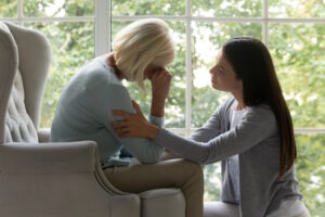 Lady soothing a crying mature woman and wondering about the reasons why you need a wrongful death lawyer.